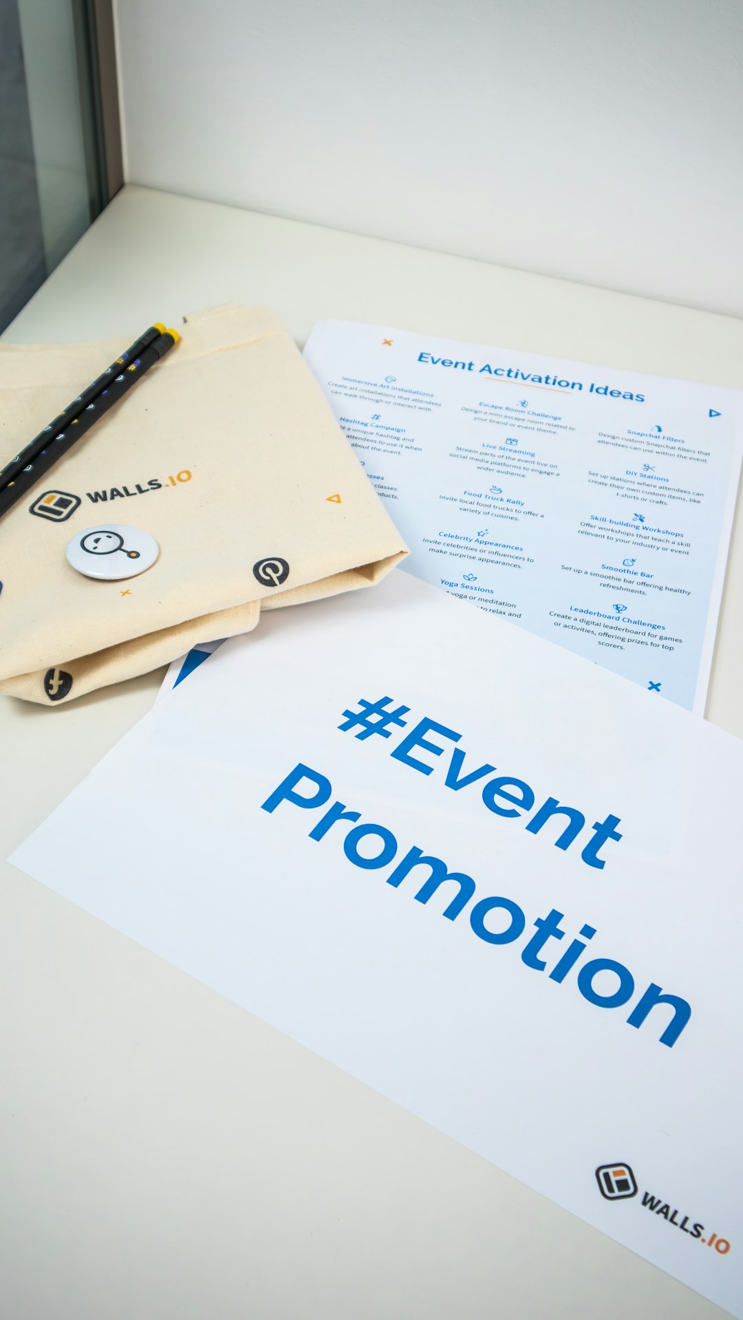 Materiel promotionnel WALLS.IO pour un evenement d'entreprise pose sur une table, avec tote bag, stylos, badge et documents de promotion.