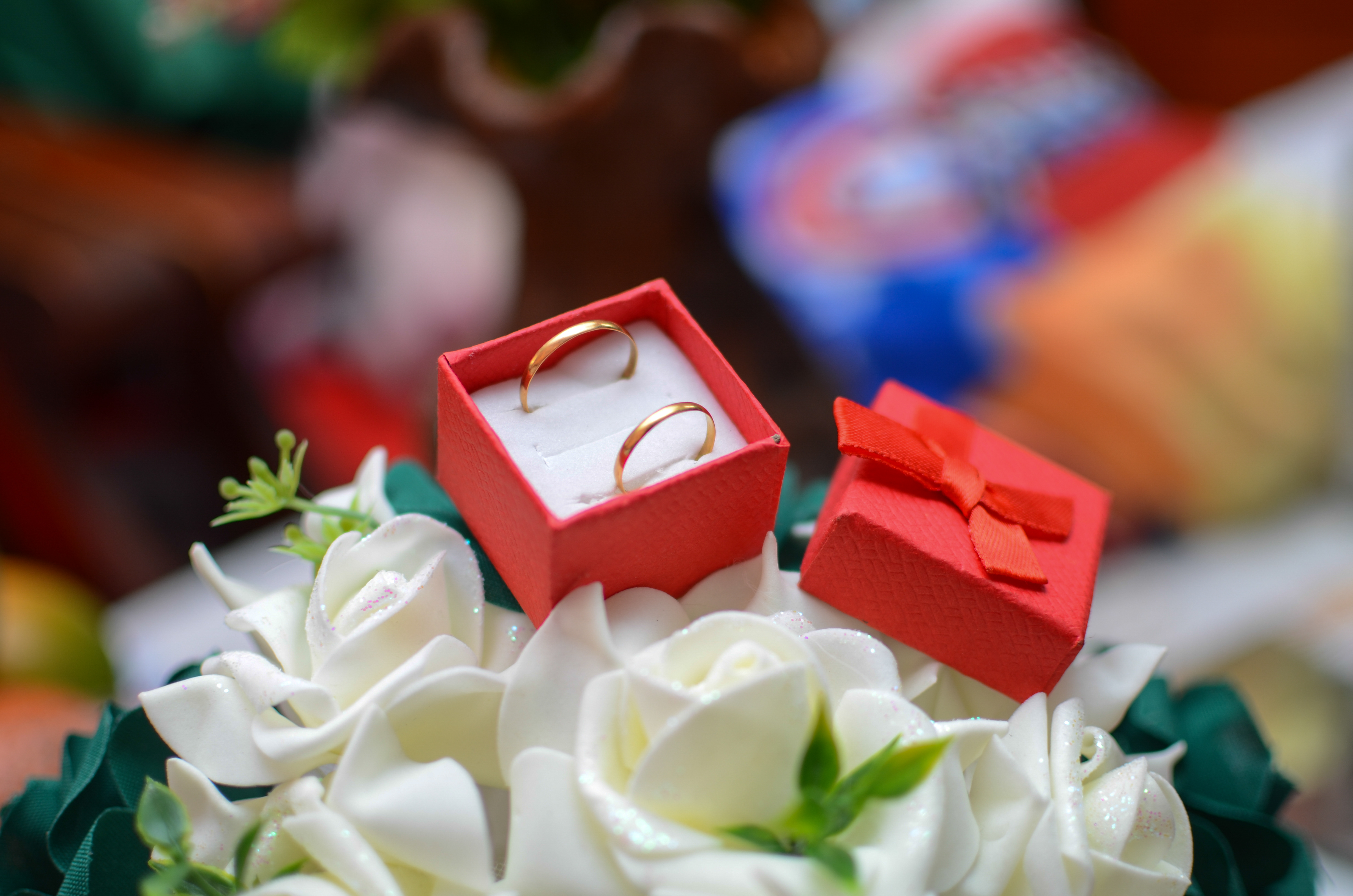 Deux alliances dorees dans une boite rouge posee sur des fleurs blanches lors d'un mariage.